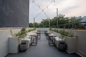 Une terrasse sur le toit, aménagée avec des tables et des jardinières, des guirlandes lumineuses, et offrant une vue sur les arbres et les bâtiments.