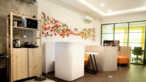 A modern office space with a wooden reception desk, a white partition, and a colorful geometric wall design. - Tuju Arteri Pods by Zuzu (Jakarta)