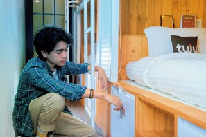 Una persona ajustando el termostato en una habitación pequeña y moderna con una cama de madera y una mesita de noche.