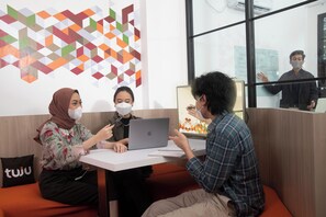 A modern interior with a geometric wall art, a white table, and orange seating. - Tuju Arteri Pods by Zuzu (Jakarta)