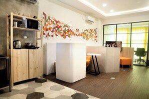 A modern office space with a kitchen area, a white reception desk, and a seating area with a yellow chair. - Tuju Arteri Pods by Zuzu (Jakarta)
