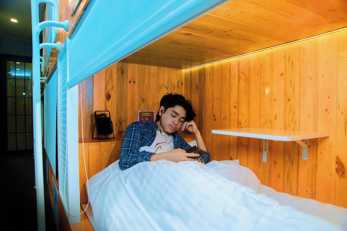 Una habitación tipo cabaña de madera con una cama, un estante y un teléfono fijo en la pared.