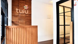 A reception area with a wooden panel design, a white brick wall, and a black-framed glass door. - Tuju Arteri Pods by Zuzu (Jakarta)