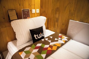 Una habitación de hotel con una cama, un cojín con la palabra "tuju" y una señal con información del hotel, todo con paredes de madera.