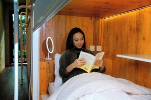 Una persona leyendo un libro en una habitación de madera con cama, mesita de noche y espejo.