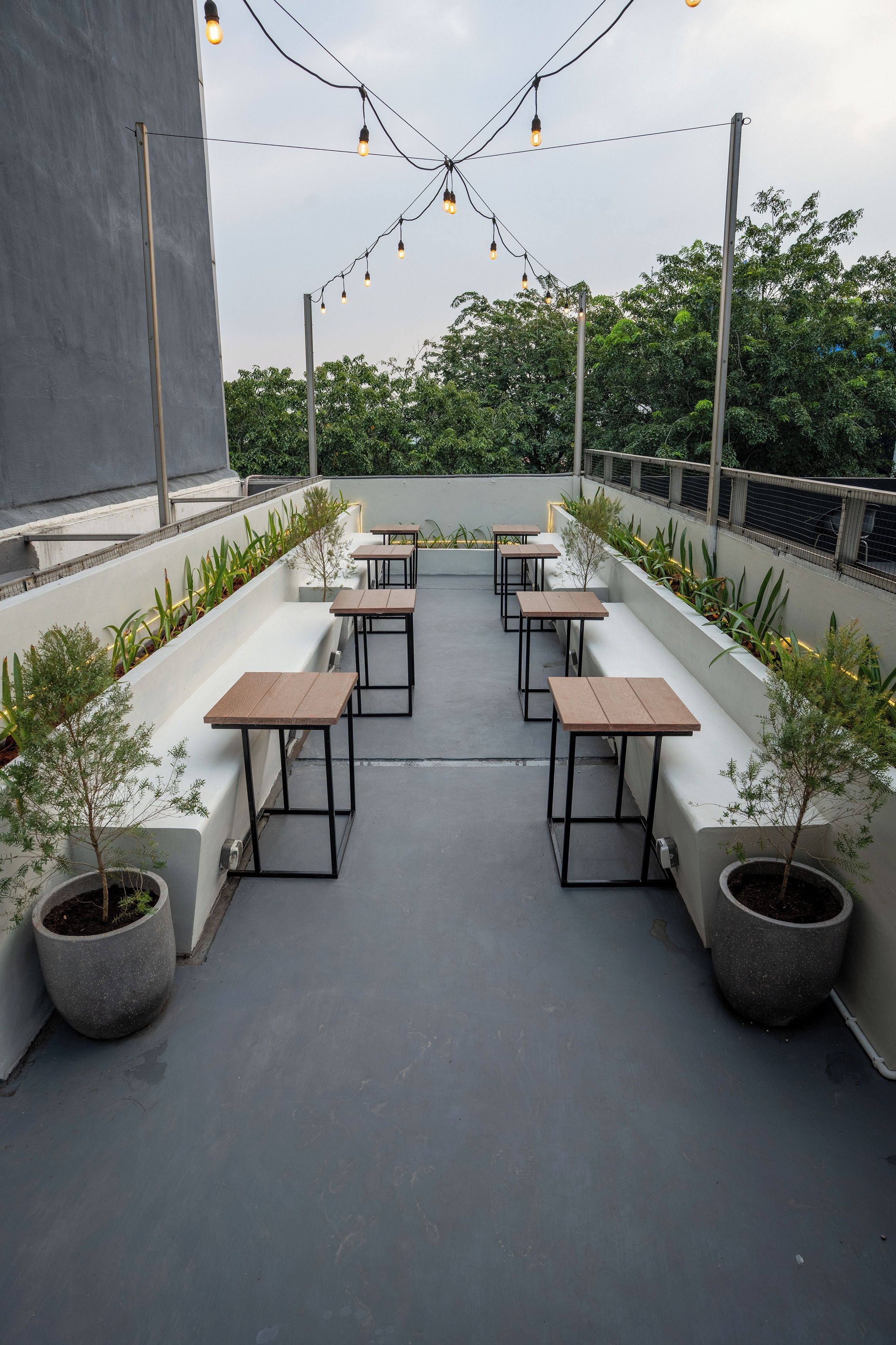 An outdoor seating area with tables and chairs, surrounded by potted plants and string lights.