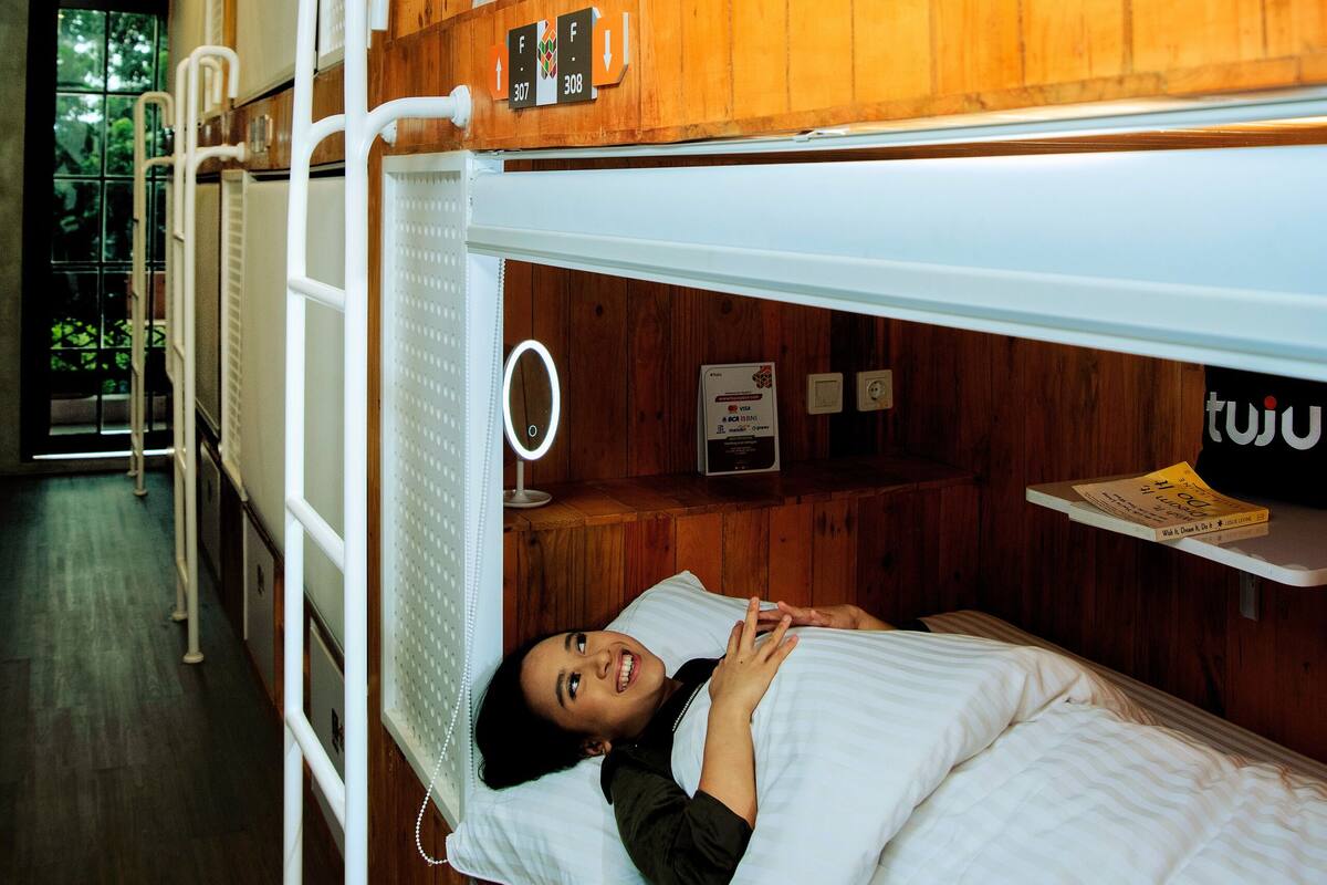 A bunk bed room with wooden walls and a white ceiling. There is a ladder attached to the bunk bed, and a small shelf with a book on it.