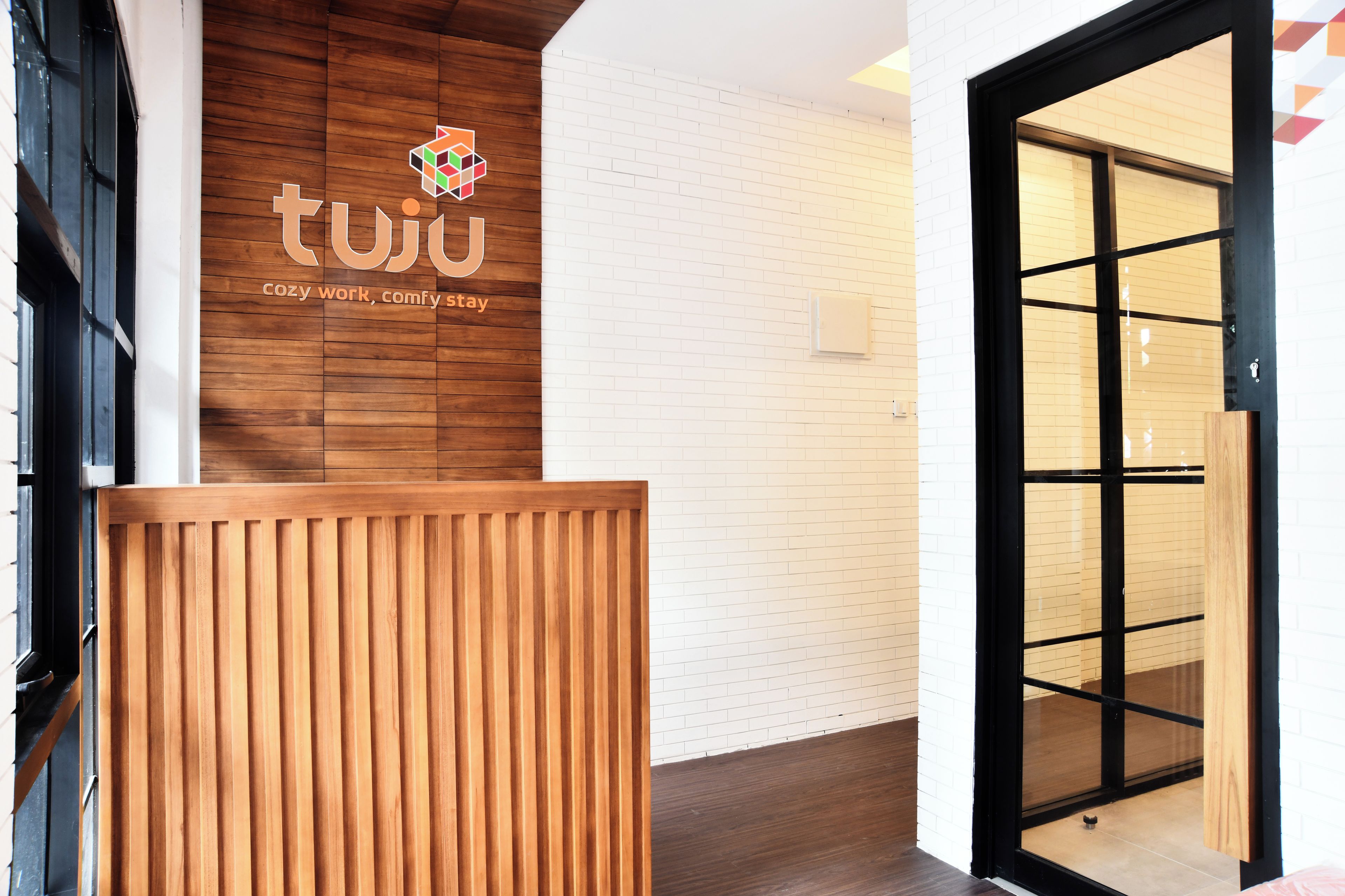 A reception desk with a logo and the text 'twu cozy work, comfy stay' against a white brick wall.