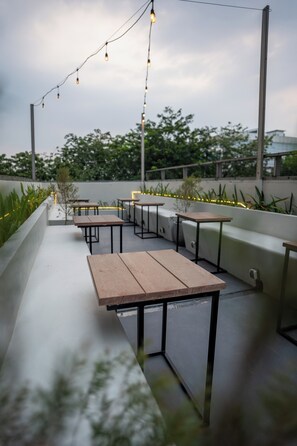 An outdoor seating area with tables and chairs, string lights, and greenery. - Tuju Arteri Pods by Zuzu (Jakarta)