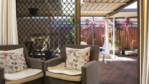 Un espacio exterior techado con mobiliario de mimbre y vistas a un jardín.