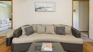 Una sala de estar con un sofá color beige, cojines estampados, una revista sobre una mesa de centro y un cuadro en la pared.
