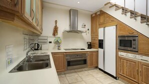 Eine kleine Küche mit Holzausstattung, einem Edelstahl-Spülbecken, einem eingebauten Backofen, einer Mikrowelle und einem Kühlschrank.