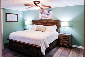 A bedroom with a wooden bed, two bedside tables, a ceiling fan, and wall art.