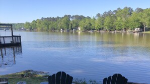 A lakeside view with three Adirondack chairs and a wooden deck.