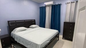 A bedroom with a bed, nightstands, a dresser, a ceiling fan, and a window with curtains. - SINGH'S APARTMENT  (Georgetown)