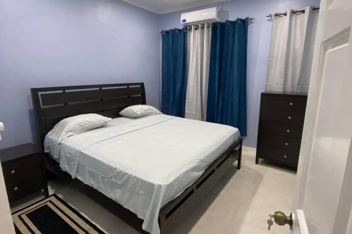 A bedroom with a bed, nightstands, a dresser, a ceiling fan, and a window with curtains.