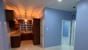 A spacious, well-lit room with a kitchen area, a dining table, and a hallway leading to another room. - SINGH'S APARTMENT  (Georgetown)