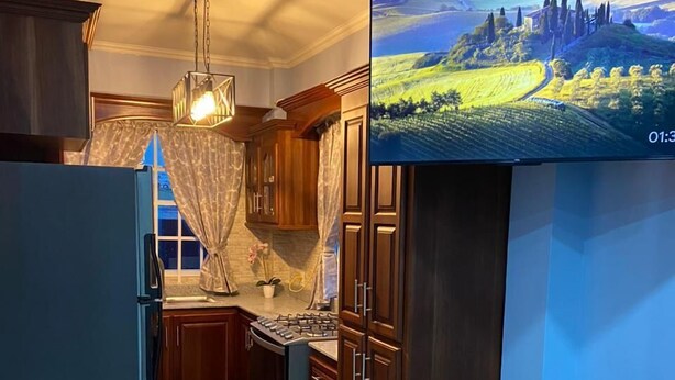 A modern kitchen with wooden cabinets, a built-in stove, and a dining area with a round table and bar stools. - SINGH'S APARTMENT  (Georgetown)