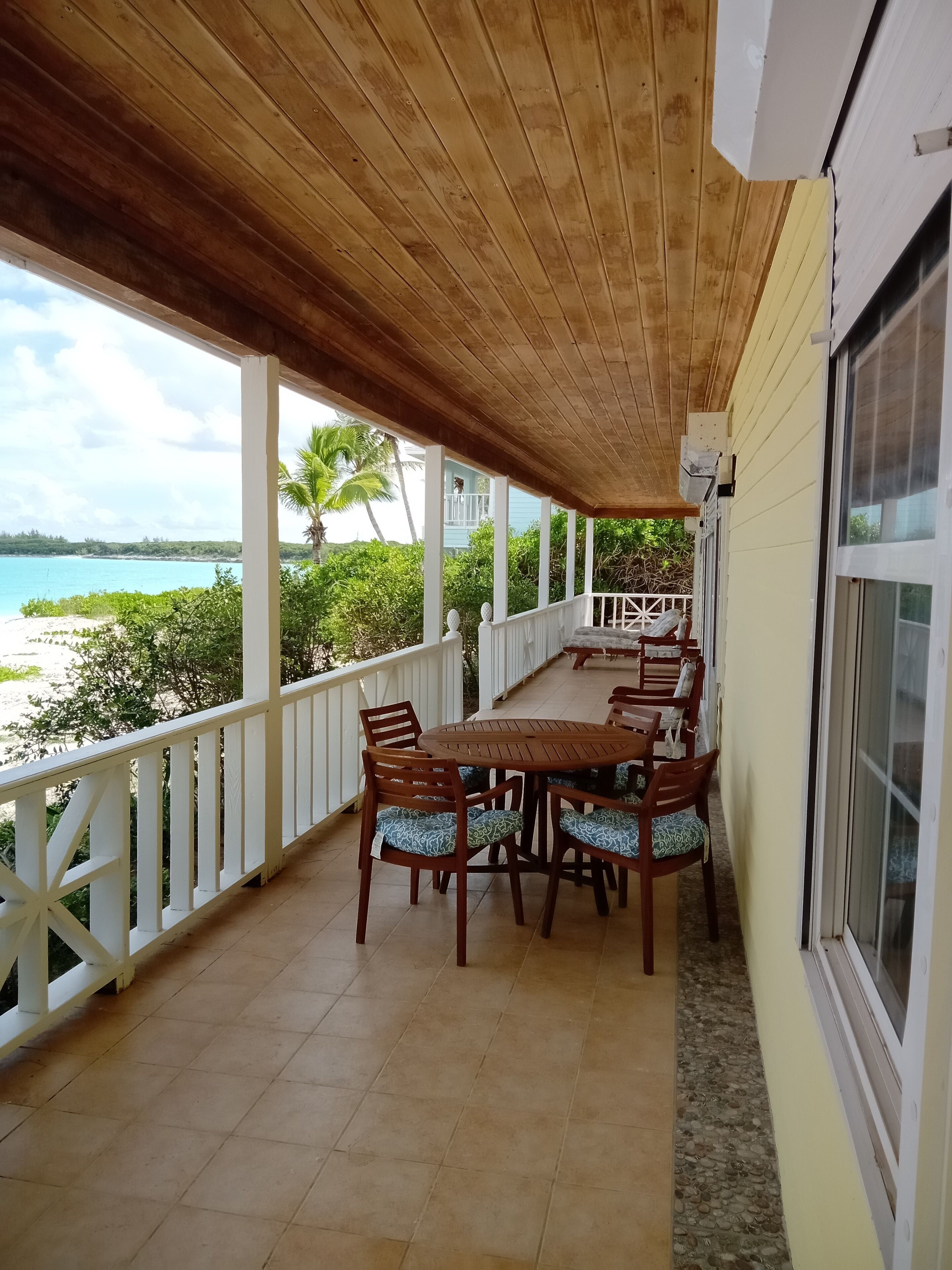 A covered patio with a wooden ceiling, white railings, and a dining table with chairs.