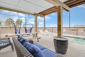 Un espacio al aire libre techado con piscina, sillas de descanso, una hamaca y una terraza de madera.