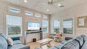 Un salon spacieux équipé d’un téléviseur, d’un ventilateur de plafond et de grandes fenêtres.