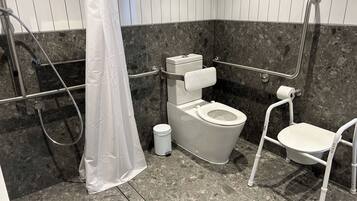 A modern bathroom with a toilet, grab bars, a shower, and a white chair.