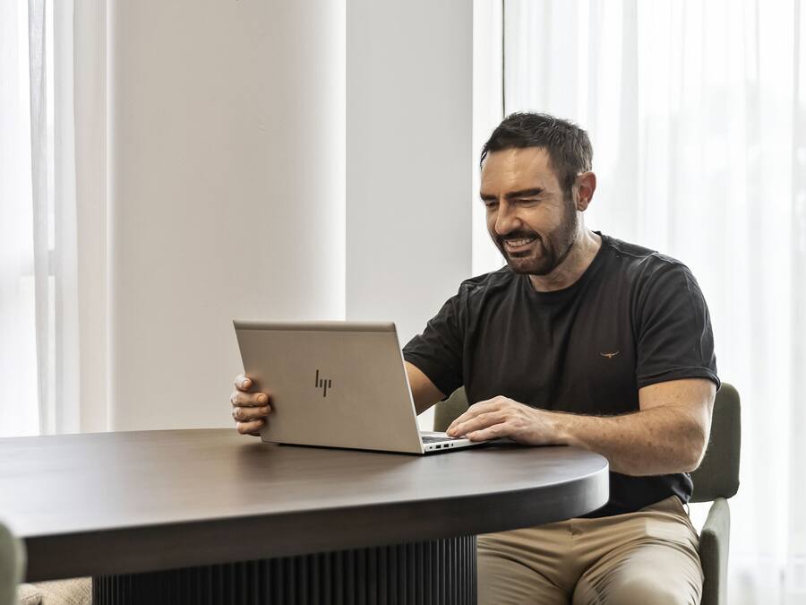 A person seated at a table with a laptop, in a room with large windows and a modern design.