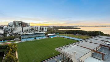 Un estadio con césped verde y asientos azules, rodeado de edificios y una masa de agua.