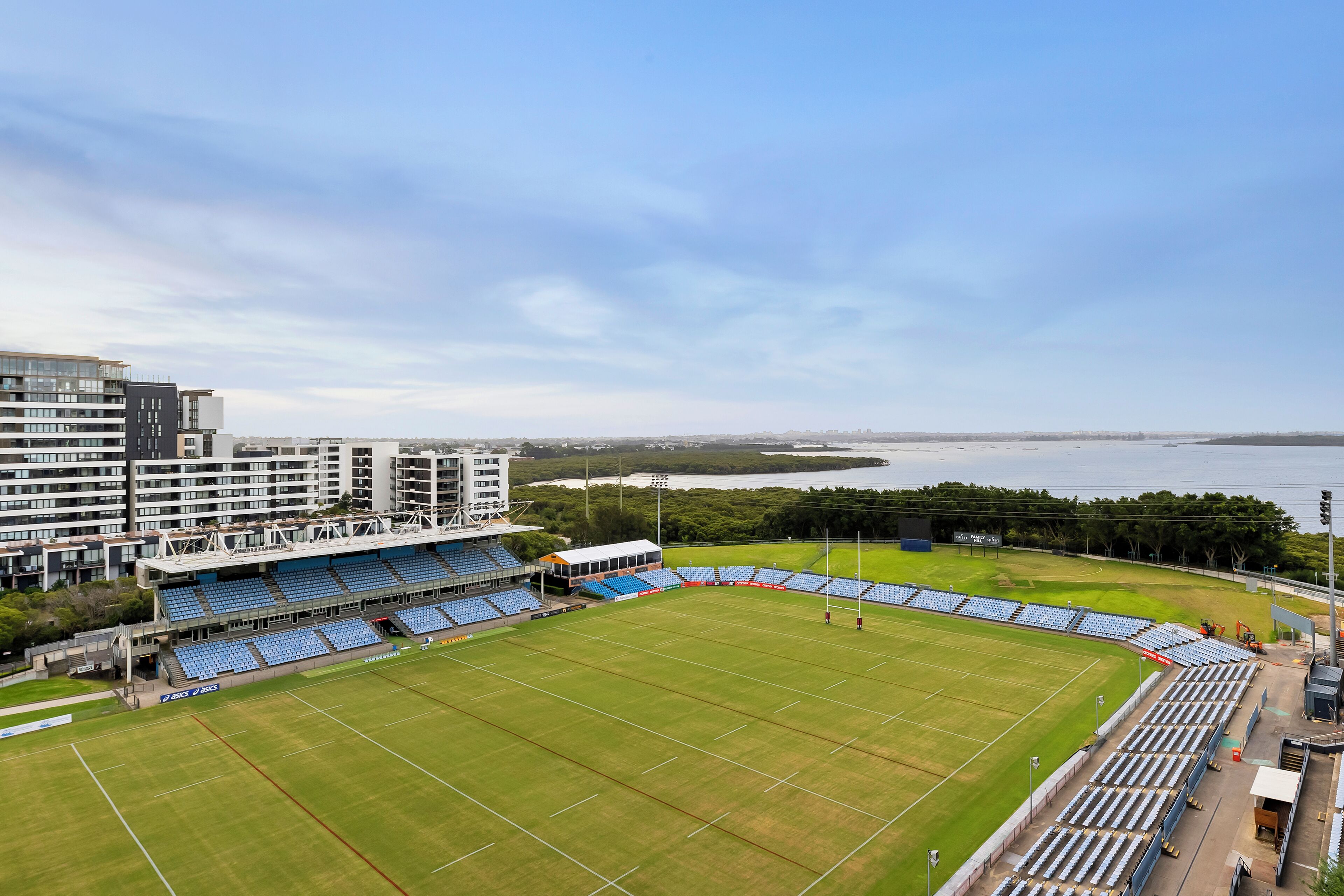 Un estadio con asientos azules, césped verde y un cuerpo de agua al fondo.