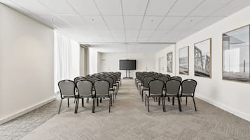 Una sala de conferències amb files de cadires, una pantalla gran i quadres als murs.