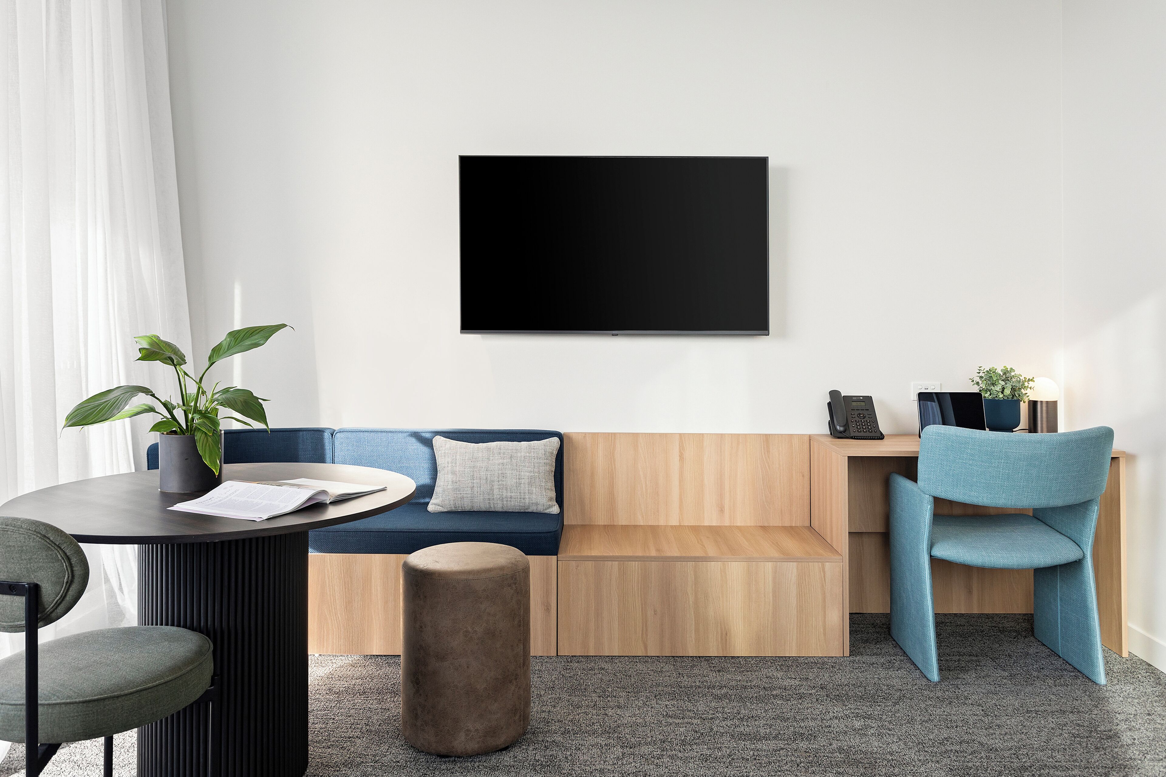 Un espace de bureau moderne avec une table ronde sombre, un canapé bleu, un bureau en bois clair, une chaise bleue et une plante en pot.