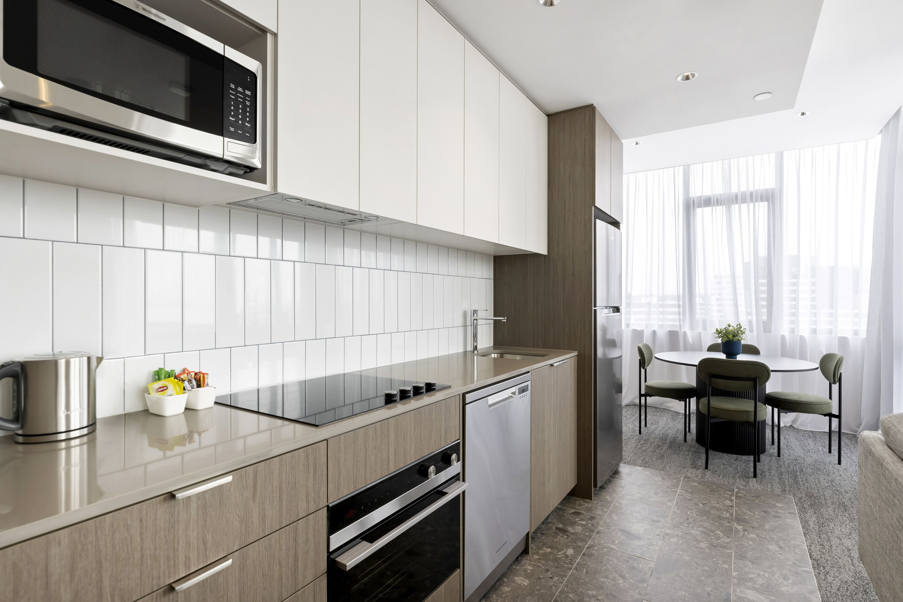 Cocina moderna equipada con microondas, horno y lavavajillas. Cuenta con un comedor con mesa y sillas, y vistas panorámicas de la ciudad a través de amplios ventanales.