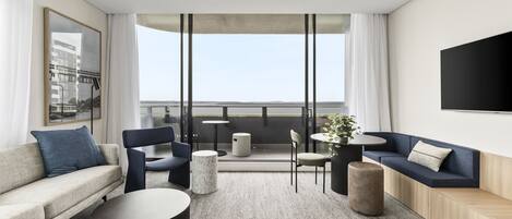 A modern hotel room with a sofa, chairs, a small table, and a balcony with a view.