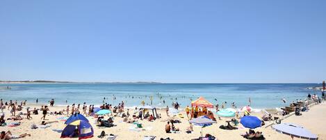 A crowded beach with people sunbathing and swimming.
