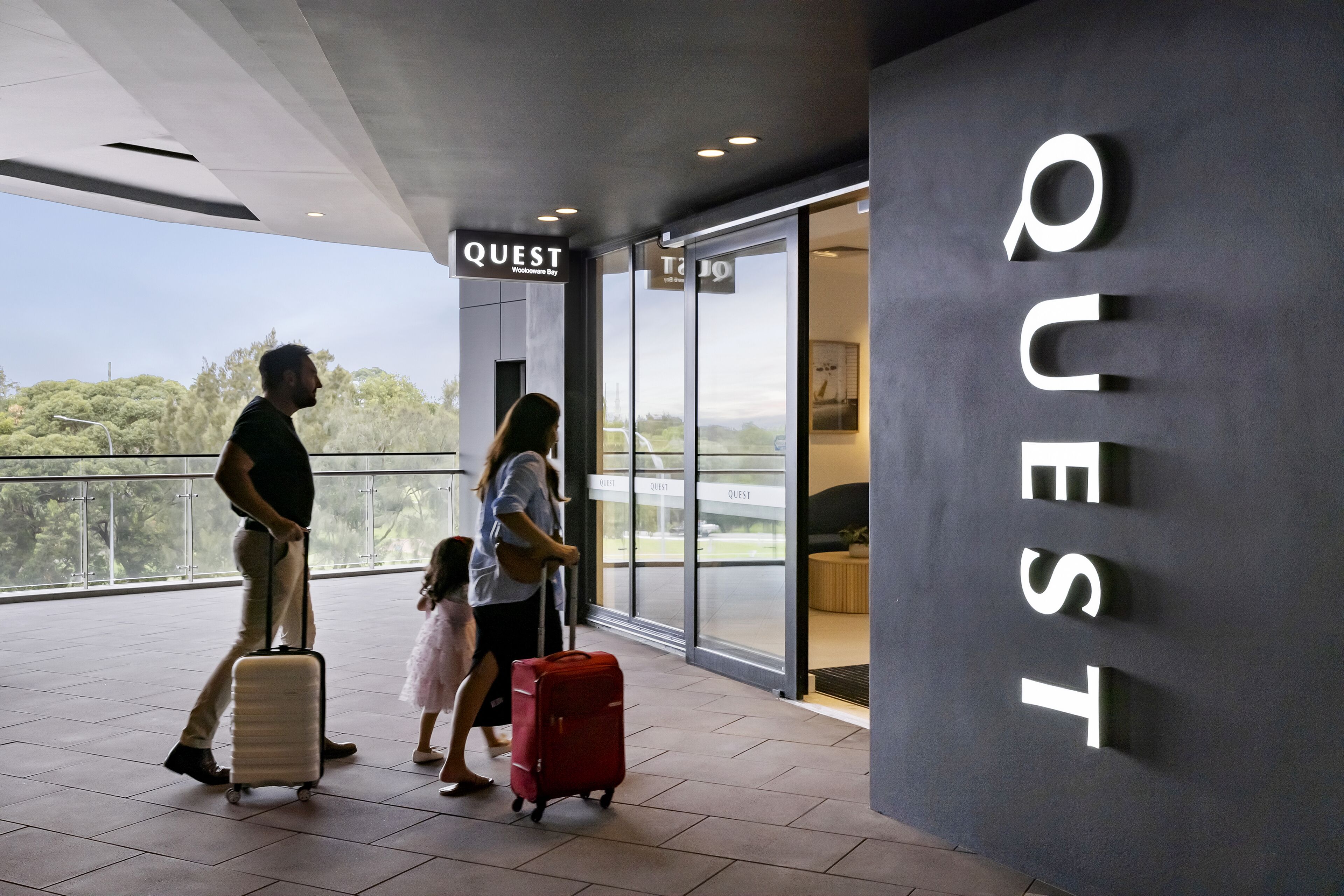 A modern hotel entrance with a large sign reading "QUEST" and a view of the outdoors.