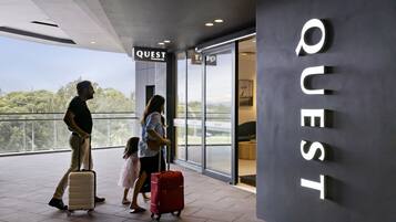 A modern hotel entrance with a large sign reading "QUEST" and a view of the outdoors.