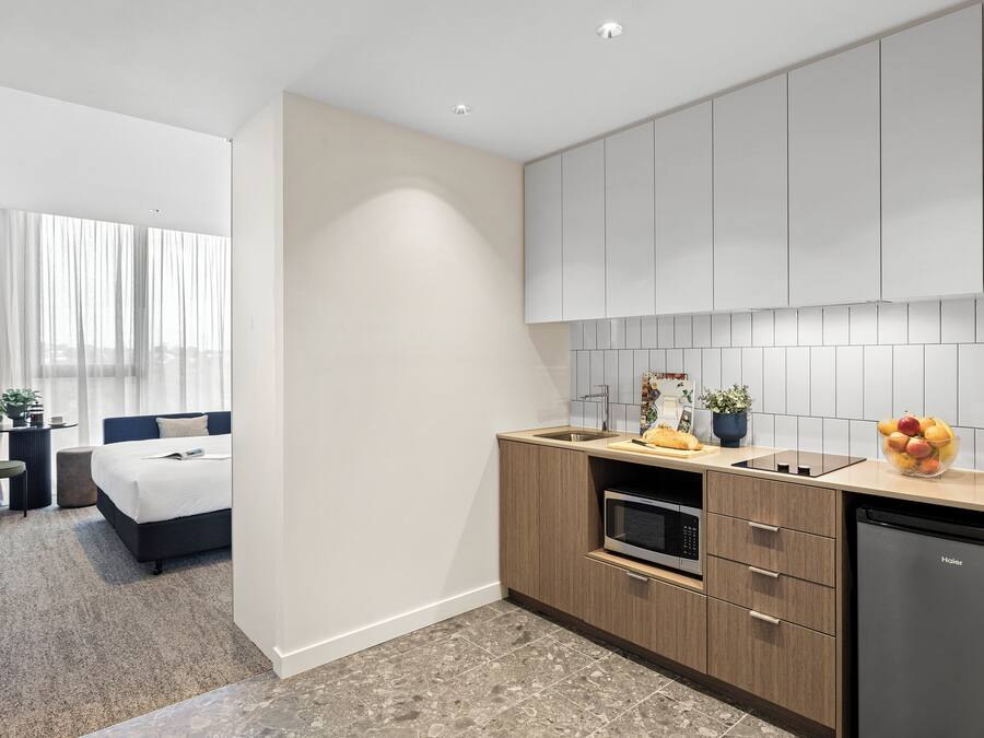 Una habitación de hotel moderna con kitchenette, una cama, un escritorio y vistas a la ciudad.