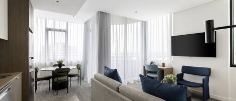 Ein modernes Wohnzimmer mit einer Couch, einem Esstisch und einem an der Wand befestigten Fernseher.