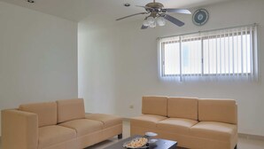 A living room with two beige sofas, a dark coffee table, a ceiling fan, and a window with blinds. - Casa Palmares - Yucatán Home Rentals (Telchac Puerto)