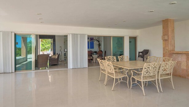 A spacious room with a large dining table and chairs, a sliding glass door leading to an outdoor area, and a stone accent wall. - Casa Palmares - Yucatán Home Rentals (Telchac Puerto)