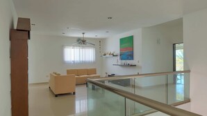 Ein geräumiger Wohnbereich mit einer Couch, einer Glastrennwand und einem Deckenventilator.