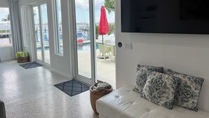 A modern living room with a sofa, a flat-screen TV, and a view of an outdoor pool area. - Waterfront oasis, sunsets, heated pool, hot tub, boat dock, near boat ramp (Bradenton)