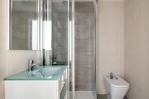 Bathroom features a glass shower enclosure, separate toilet area, and a glass sink with a chrome faucet.
