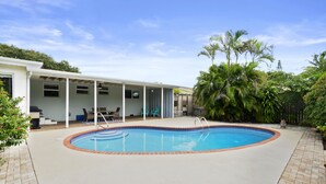A swimming pool with a tiled edge, surrounded by a patio area with chairs and a covered seating area. - Jungle house Heated Salt pool, 5 min away from the beach! (Boynton Beach)