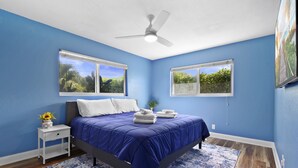 A bedroom with a bed, a nightstand, a ceiling fan, and two windows. - Jungle house Heated Salt pool, 5 min away from the beach! (Boynton Beach)