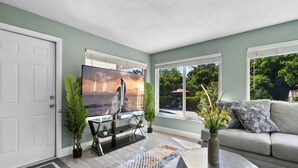 A living room with a television, a sofa, a coffee table, and a view of the outdoors. - Jungle house Heated Salt pool, 5 min away from the beach! (Boynton Beach)