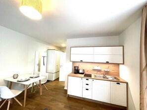 Een compacte kitchenette met een ingebouwde oven, een koffiezetapparaat en een spoelbak. Er is een klein zithoekje met een tafel en stoelen.