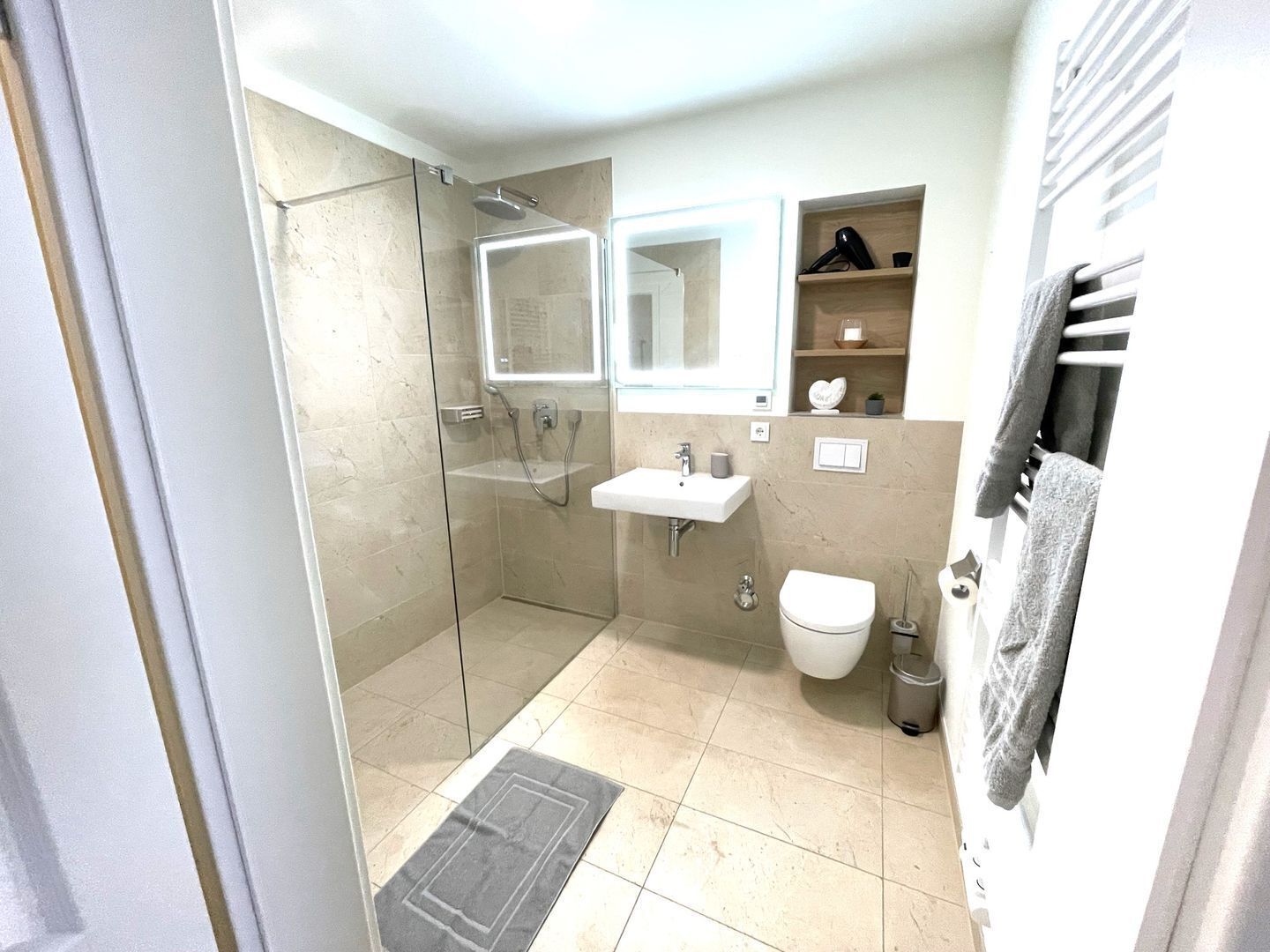 Une salle de bain moderne avec une douche à parois de verre, un lavabo avec un miroir au-dessus, des toilettes et un porte-serviettes.