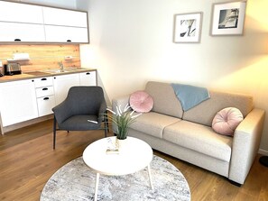 A modern living room with a grey armchair, a beige sofa with decorative pillows, a white coffee table, and a round rug.