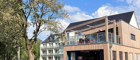 A modern building with a wooden facade, outdoor seating, and a clear blue sky.